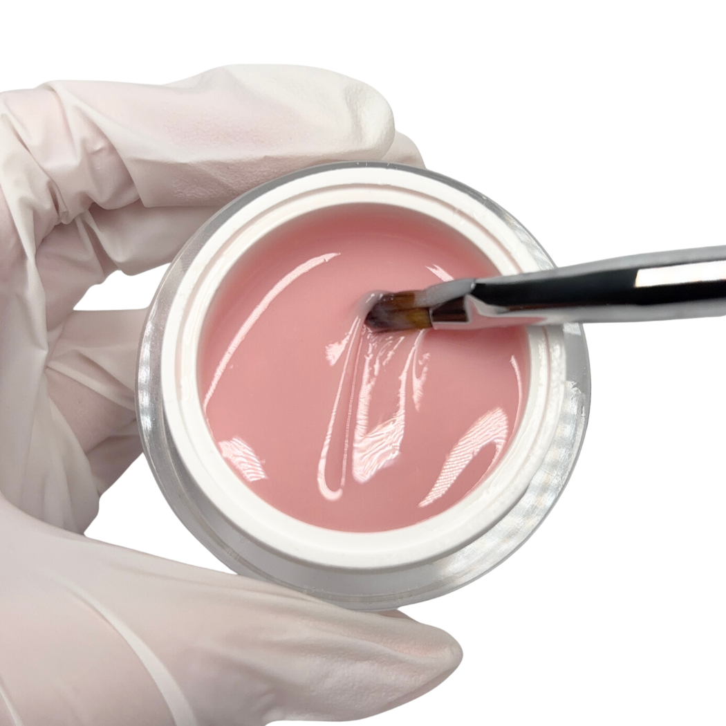 Pink gel in a container with a brush and gloved hands on a white background